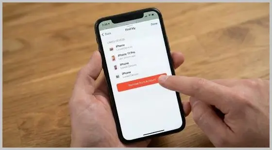 Hand holding an iPhone displaying the iCloud Find My app with the Remove from Account button highlighted.
